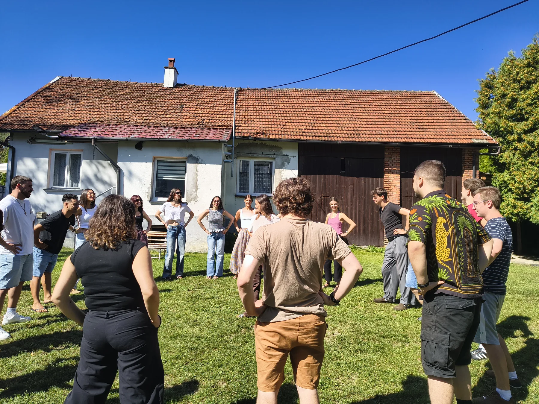 Uczestnicy stoją w kręgu przed domem